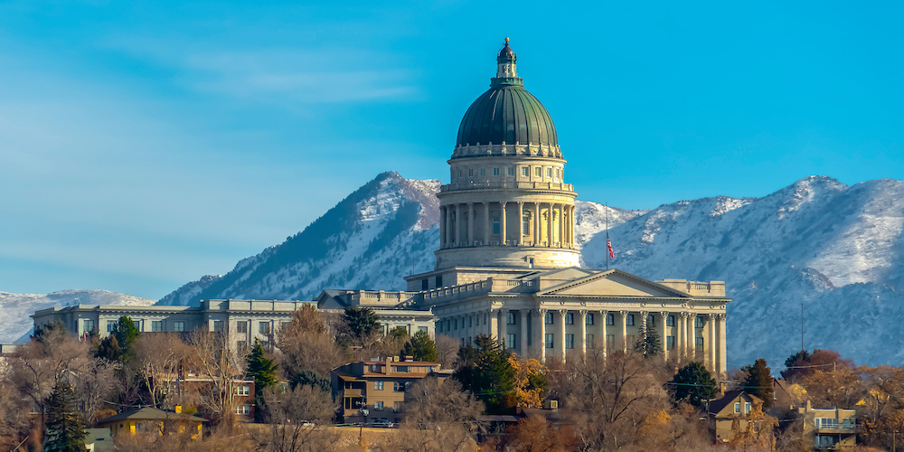 Utah State Capital Building viewed on a sunny day. The grand Utah State Capital Building towering over Salt Lake City. A scenic view of snowy mountain and blue sky can be seen in the background.